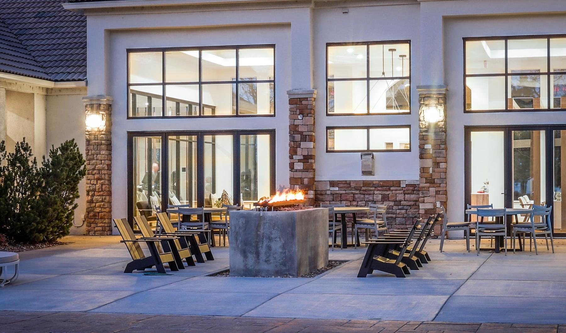 The essence of exceptional living Legacy at Highlands Ranch's patio has a fire pit, Adirondack chairs, and warmly lit windows, creating a cozy evening ambiance.